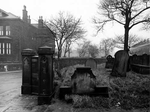 This photo shows part of the graveyard belonging to St Bartholomew's Church on the corner with Church Road and Strawberry Lane. The main entrance is visible in the foreground but the gate is no longer there. Houses and trees are visible. Pictured in December 1947.