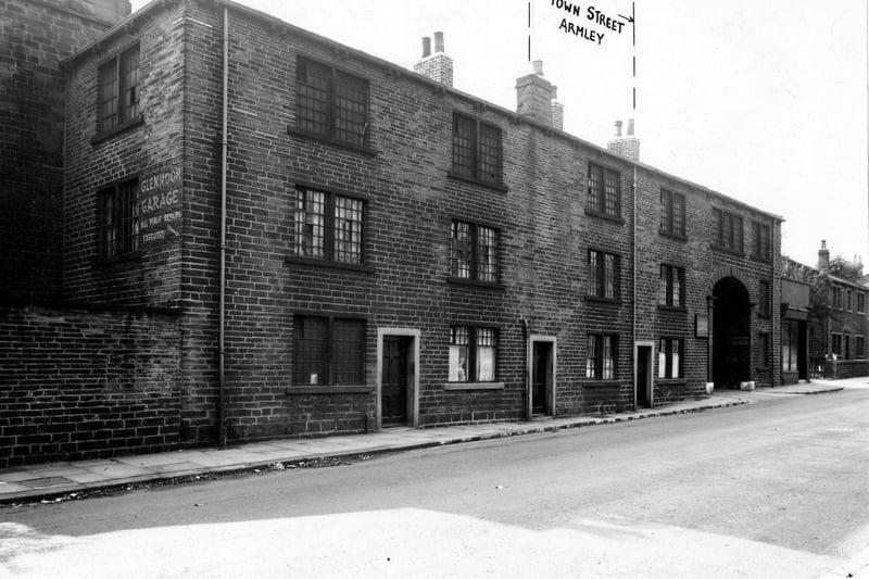  Town Street with the arched entrance to Glenmoor Garage, owned by A. Haywood and Sons, on the right. A sign for the garage is painted on the end of number 153. A manhole cover is visible. Pictured in September 1947.