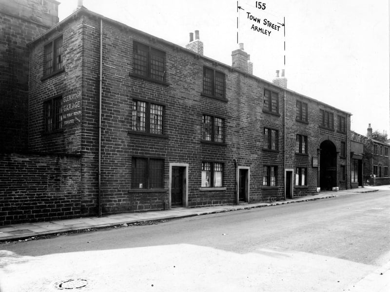 Town Street with the arched entrance to Glenmoor Garage, owned by A. Haywood and Sons, on the right. A sign for the garage is painted on the end of number 153. A manhole cover is visible. Pictured in September 1947.
