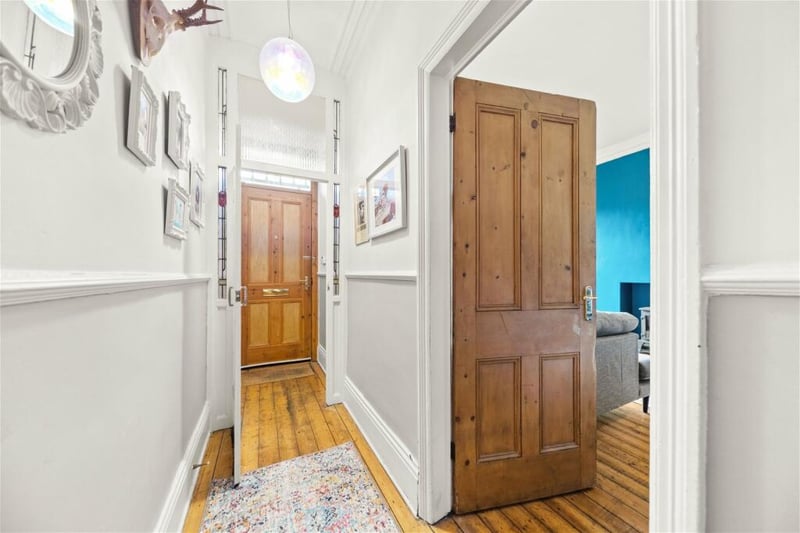 Enter into a hallway with wooden floors and stairs leading to the upper floors.