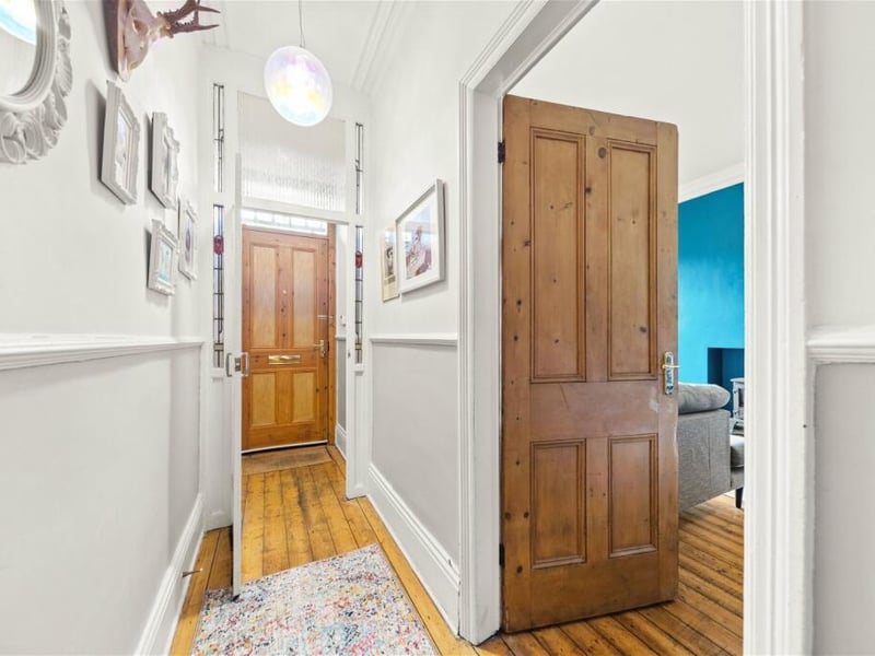Enter into a hallway with wooden floors and stairs leading to the upper floors.