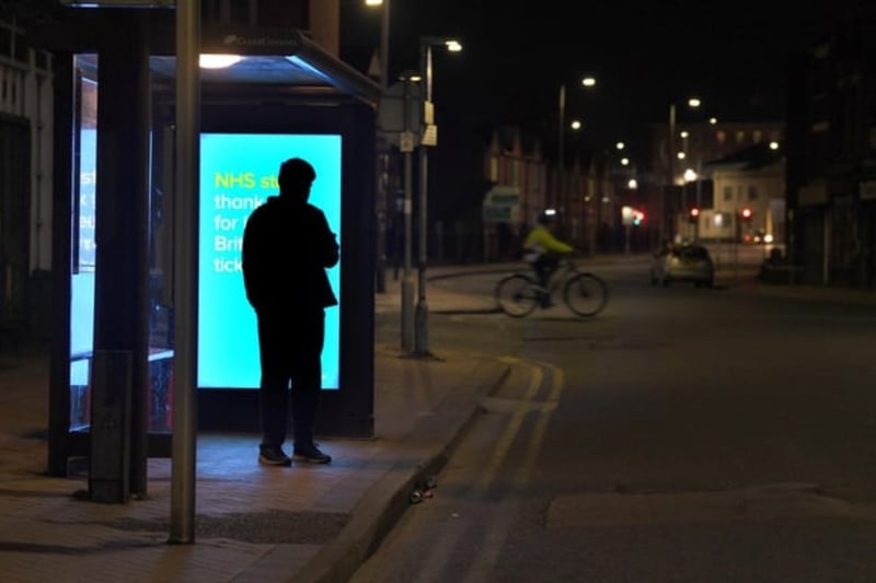 One lone traveller waiting at the bus stop, with a thank you NHS billboard behind him.