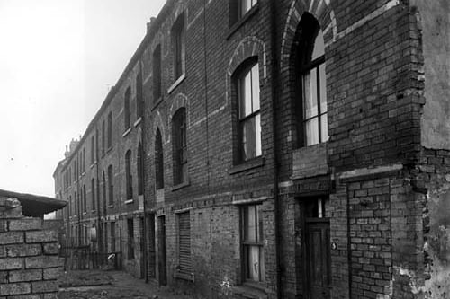 Back-to-back terraced buildings at the rear of Garr's Terrace in November 1958. The ginnel on the right of number 5 has been sealed off while the one between numbers 11 and 13 is still open and allows access from Garr's Terrace. Each property has a small grassed area with a shared outside toilet (visible on the left) located at the end of the garden. A tin bath is visible hung on the exterior wall of number 21 on the left.