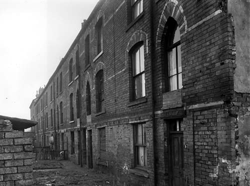 Back-to-back terraced buildings at the rear of Garr's Terrace in November 1958. The ginnel on the right of number 5 has been sealed off while the one between numbers 11 and 13 is still open and allows access from Garr's Terrace. Each property has a small grassed area with a shared outside toilet (visible on the left) located at the end of the garden. A tin bath is visible hung on the exterior wall of number 21 on the left.