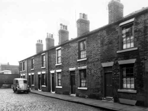 Single fronted back-to-back houses on Chambers Street, numbers run from 22 to 12, left to right. Across the wall on the left edge is a Leeds Corporation bus depot. A royal mail delivery van is parked outside number 20 Chambers Street. Pictured in October 1958.