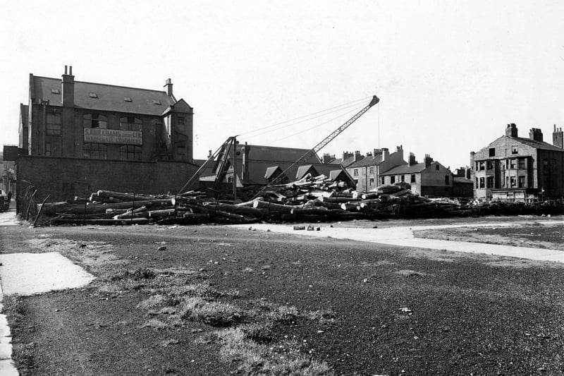 On the left is S. Abrahams (Leeds) Ltd., Wholesale Clothiers at no. 31 Concord Street. To the right is a row of terraced houses; the ones on the right have broken windows. Far right is Skinner Lane. In the middle is a lumber yard with a crane. In the foreground is waste ground. Pictured in September 1950
