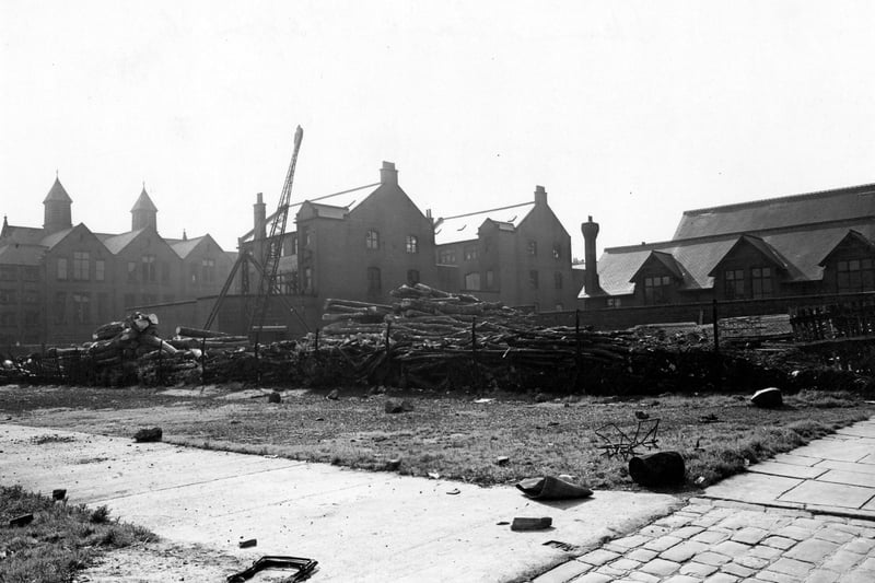 On the left is S. Abrahams (Leeds) Ltd., Wholesale Clothiers at no. 31 Concord Street. To the right is a row of terraced houses; the ones on the right have broken windows. Far right is Skinner Lane. In the middle is a lumber yard with a crane. In the foreground is waste ground. Pictured in September 1950.