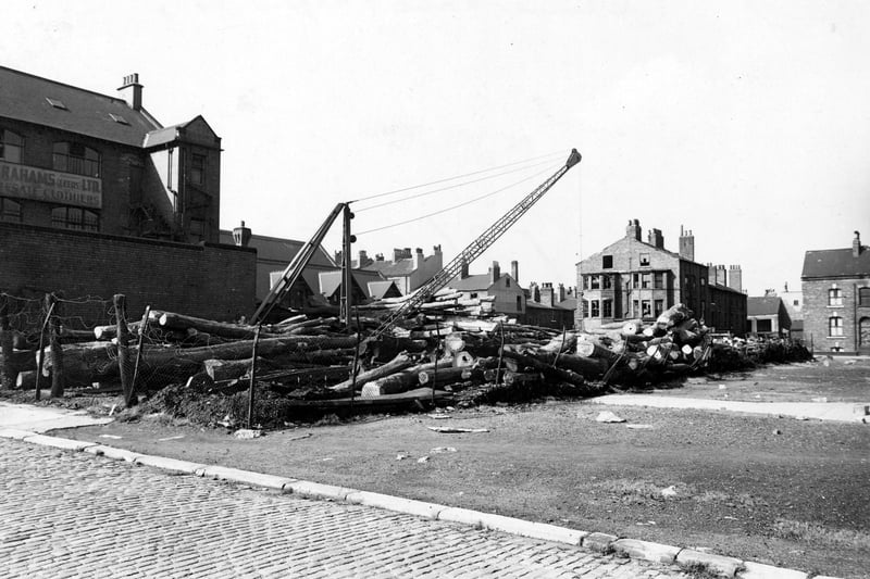 Looking north from Concord Street to Skinner Lane in September 1950. On the left is Abrahams, Wholesale Clothiers at no.31 Concord Street. In the middle and on the right are some terraced houses, some have broken windows. In the middle is a lumber yard with a crane in it. In the foreground is a cobbled street and waste land.