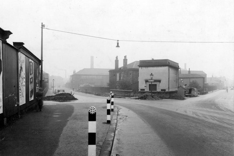 Crown Point Road looking south south west at the junction with Black Bull Street. Advertising hoardings on the left. Street light suspended on wire between two poles on either side of the street. Several striped bollards with reflectors on top positioned at the edge of the pavement. The premises of Edward Bidgood & Co, Black Bull Street can be seen in the distance on the left. Pictured in October 1953.