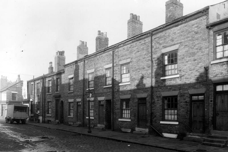 Back-to-back terraced houses on Derby Crescent pictured in October 1958. Between houses 37 and 39 and 41 and 43 there are ginnels giving access to gardens on Derby Terrace. On the far left a removals van is parked outside number 35 while a sofa is being manhandled down some cellar stairs.