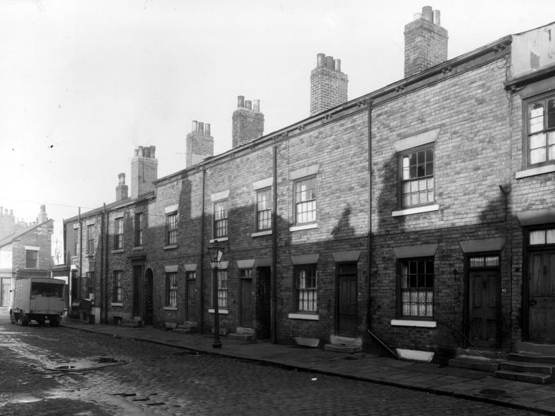 Back-to-back terraced houses on Derby Crescent pictured in October 1958. Between houses 37 and 39 and 41 and 43 there are ginnels giving access to gardens on Derby Terrace. On the far left a removals van is parked outside number 35 while a sofa is being manhandled down some cellar stairs.