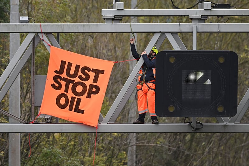 An activist puts up a banner reading "Just Stop Oil" atop an electronic traffic sign along M25 