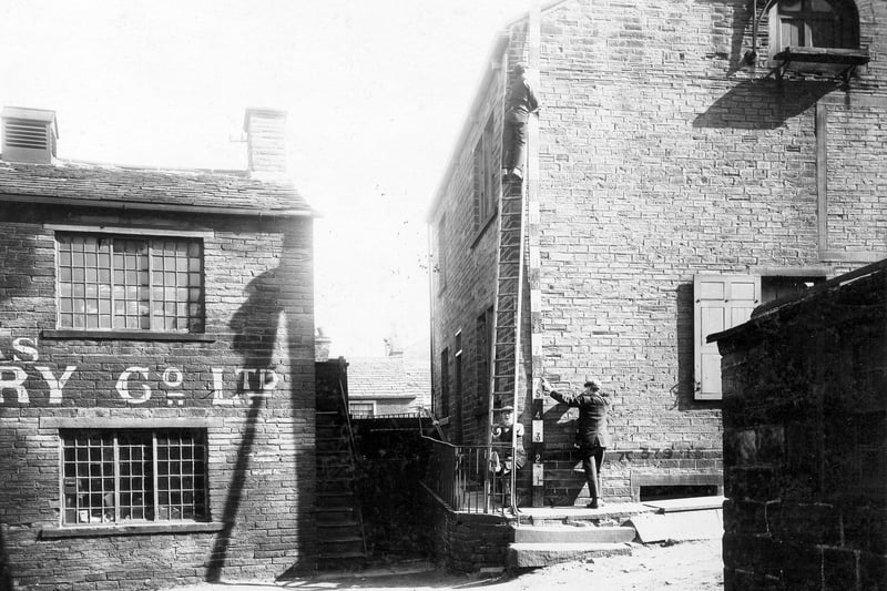 The back of premises on Town Street in 1909. To the right is a building with a door and platform in upper storey. Workmen can be seen holding ladder and measuring pole at side of building. To the left is the Sanitas Steam Laundry, 126 Town Street.