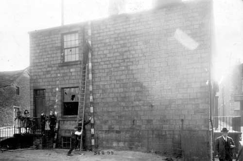 Town Street in May 1909. The rear view of property which was to be demolished. The site was used for a new Poor Rate Office. A small group of children on the left are watching workmen measuring the building.