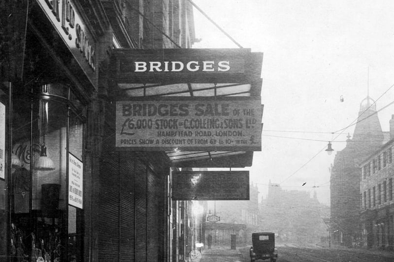 This photo shows part of Marks and Spencer Ltd, who were listed at 76 Briggate, then shown is Bridges, Drapers with sign: 'Bridges sale of the £6,000 stock of C.Coleing and sons Ltd, Hampstead Road. Prices show a discount of from 6/8 to 10/- in the £' in the distance a sign for Warwickshire furnishing Co Ltd is visible. Pictured in March 1930.