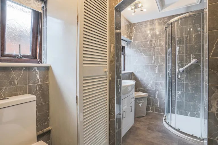 The fully tiled house bathroom comprises a walk-in shower cubicle, wash basin, WC and heated towel rail.