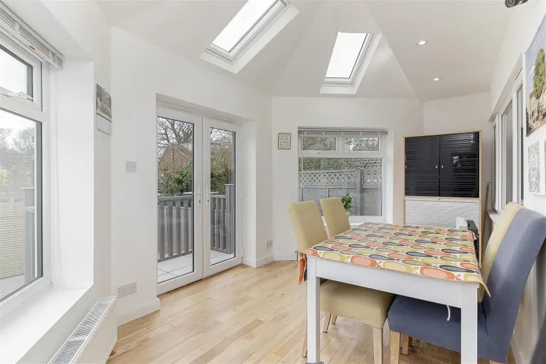 Here is a bright dining space with panoramic views and skylight windows. French doors overlook the rear garden.