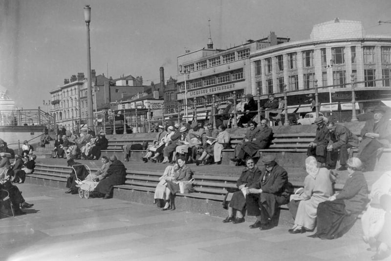 Locals and visitors enjoying a spell of sunshine on the Promenade close to Church Street, Blackpool in 1959. Landmarks in the backgrund include l-r The Clifton Hotel, Robert's Oyster Rooms The Savoy Cafe complex and Burtons menswear shop