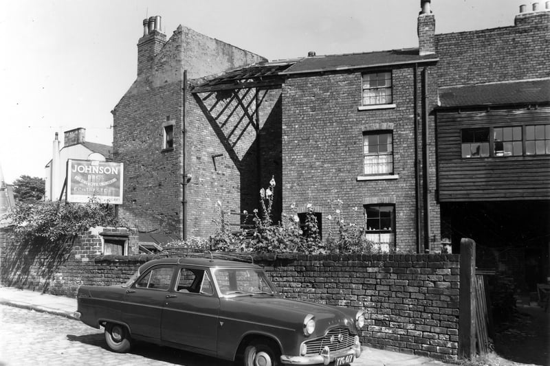 To the right of this view is the entrance to a yard outside number 20 West End Terrace, the premises of Johnson Bros, building contractors. In the background to the left is the back of number 20 Cliff Road with the back entrance to number 19 in the centre. A car is parked in the road. Pictured in August 1961.