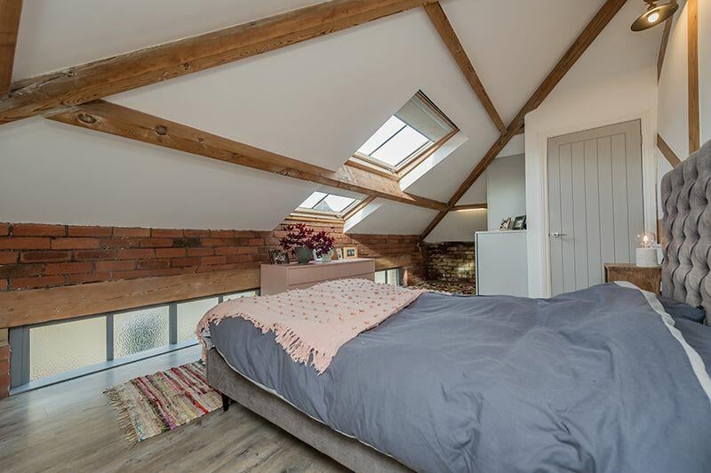 This bedroom with skylight features beautiful exposed ceiling beams and brick wall.