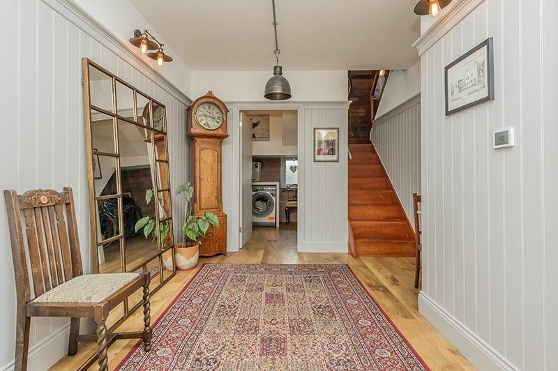 The double wood front doors open into this spacious hallway with painted wood panelling walls and industrial style lighting.