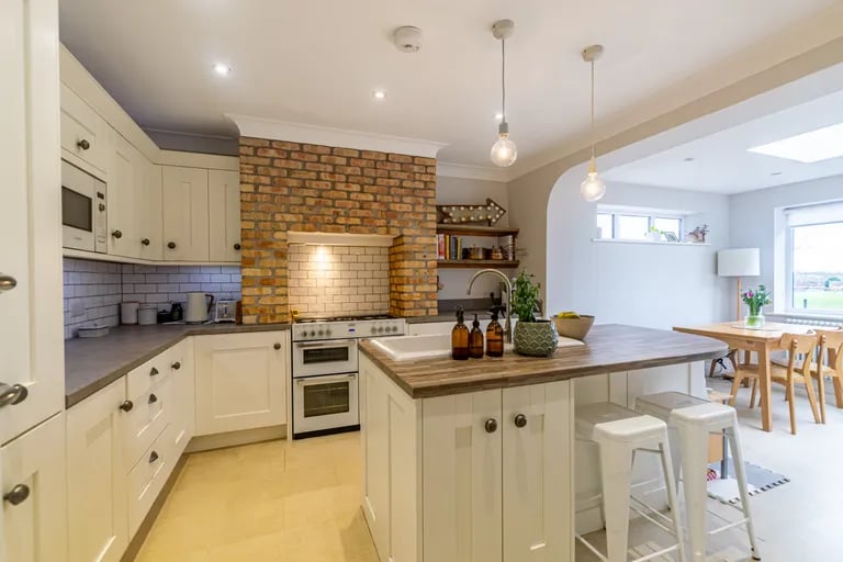 The luxurious kitchen features a large central island and an oven in an exposed brick chimney breast.