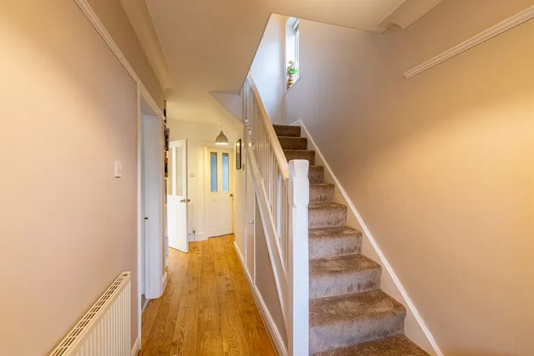 Enter into a spacious hallway with stairs to the first floor and wooden flooring.
