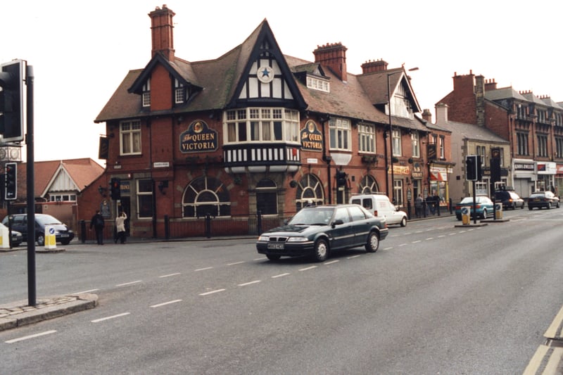  A 1998 photograph of The Queen Victoria pub at the junction of Gosforth High Street and Church Road. The photograph has been taken from the opposite side of the High Street looking towards The Queen Victoria pub and the shops beyond. The front and the side of the pub can be seen. In the foreground cars are travelling along the High Street.