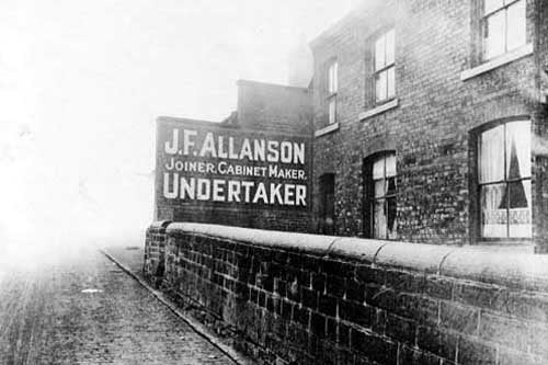 The Old Guard House on Barrack Road in December 1926. Net curtains in windows. Sign for J F Allanson, joiner, cabinet maker, undertaker on wall adjoining house.