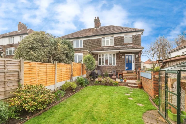 To the rear is a sprawling green garden with planted borders.