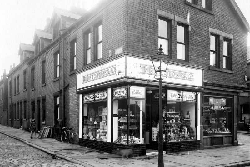 Morris Lane in September 1935. On the left is Station Parade, number 12 is a branch of Thrift Stores, grocers. Windows display a variety of goods, hardware and household wares, bread and cakes, bacon and tinned foods. Customers are offered free insurance and loyalty bonus of 2/6d (Twelve and half pence) for every £1 spent. On the right, number 10 is William Greaves, butcher.