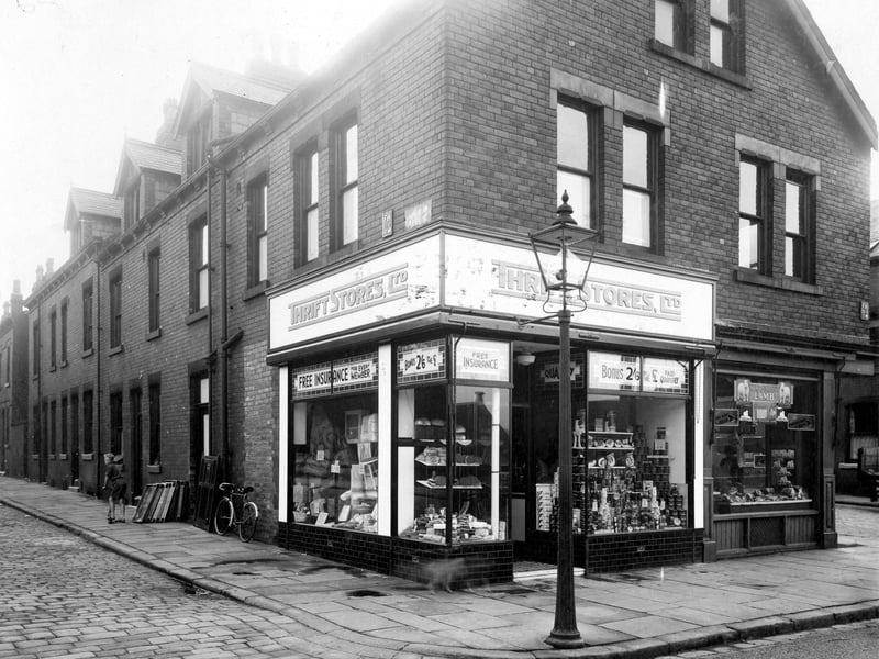 Morris Lane in September 1935. On the left is Station Parade, number 12 is a branch of Thrift Stores, grocers. Windows display a variety of goods, hardware and household wares, bread and cakes, bacon and tinned foods. Customers are offered free insurance and loyalty bonus of 2/6d (Twelve and half pence) for every £1 spent. On the right, number 10 is William Greaves, butcher.