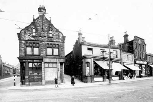 Midland Bank on corner then road which is Pratts Row. A further row of shops with Perkins Bros Plumbers at number 7 Commercial Road, and Thrift Stores at number 9. A traffic light can be seen at junction where Kirkstall Lane meets Commercial Road. Pictured in July 1938.