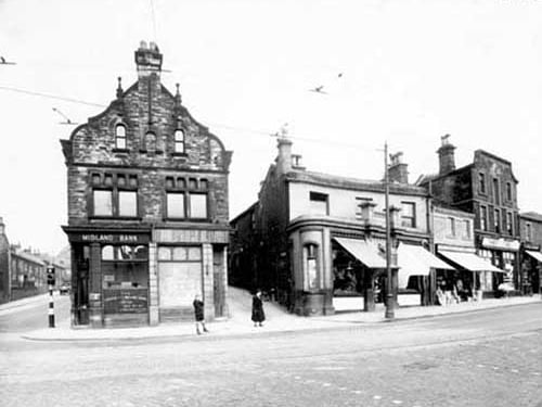 Midland Bank on corner then road which is Pratts Row. A further row of shops with Perkins Bros Plumbers at number 7 Commercial Road, and Thrift Stores at number 9. A traffic light can be seen at junction where Kirkstall Lane meets Commercial Road. Pictured in July 1938.