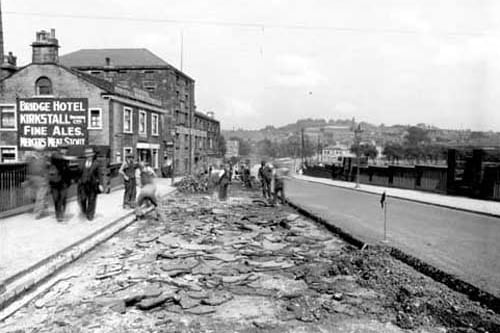 resurfacing of Kirkstall bridge. Several men are working on the road, which is partially dug up. The Bridge Hotel is on the left hand side. Pictured in June 1938.