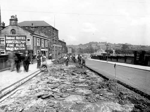 resurfacing of Kirkstall bridge. Several men are working on the road, which is partially dug up. The Bridge Hotel is on the left hand side. Pictured in June 1938.