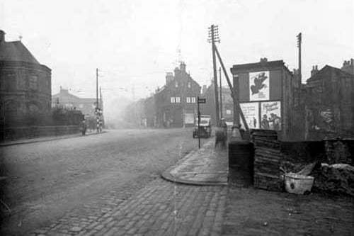 A view from Bridge Road toward junction with Abbey Road (Left 7, Kirkstall Lane) and Commercial Road to the right. The Police station is on the left in centre of photograph. Midland Bank can be seen on corner (this is number 1 Commercila Road, Manager Ernest Palmer). A Leeds City Transport bus stop is visible on the right. Pictured in January 1937.