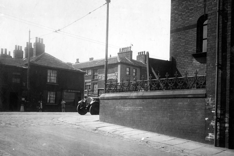 Town Street, in the centre number 33 George Barker fishmonger. Gap in buildings is Albion Place then number 37 is Alfred Dunham joiner and undertaker. There is a painted sign on the wall. A car is parked in front of the Wesleyan Chapel. The street in the foreground is Wesley Street. Pictured in July 1929.