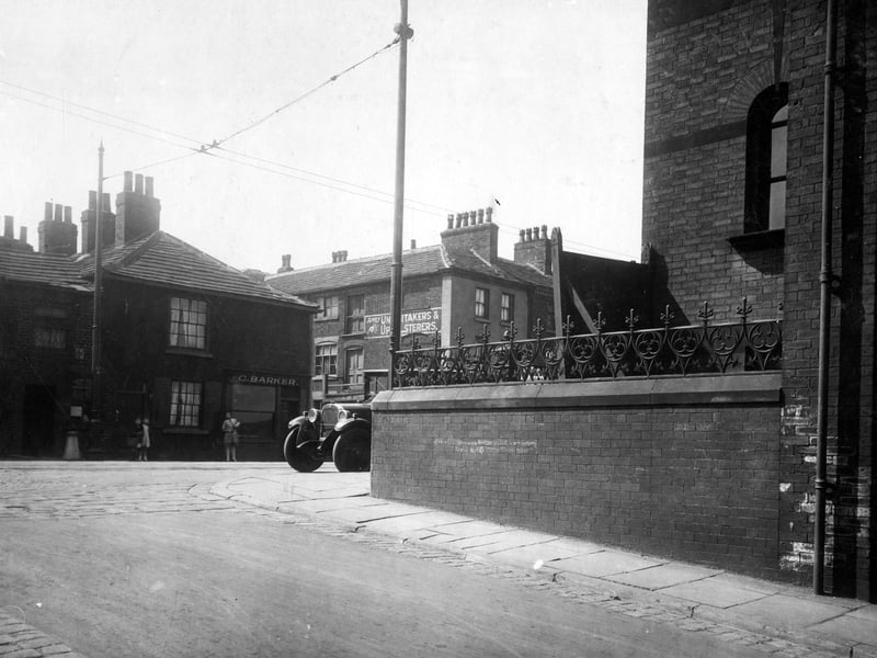 Town Street, in the centre number 33 George Barker fishmonger. Gap in buildings is Albion Place then number 37 is Alfred Dunham joiner and undertaker. There is a painted sign on the wall. A car is parked in front of the Wesleyan Chapel. The street in the foreground is Wesley Street. Pictured in July 1929.