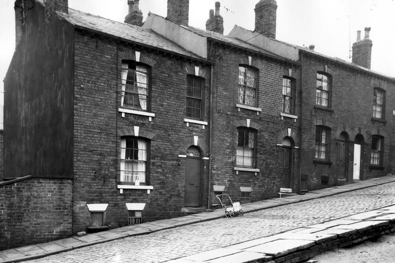 This view looks from space created from this demolition of numbers 16 and 18 Cayton Street onto numbers 13 to 19, left to right. Included in slum clearance plans for Armley Road area. Pictured in March 1964.