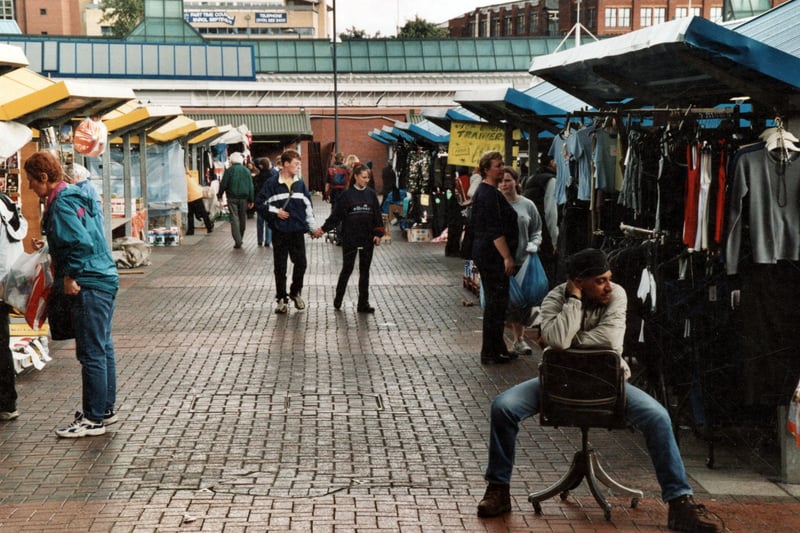 Looking down these two rows of stalls in the outdoor section we see several stalls. The only one recognisable being the clothes stall on the right. The City Bus station and the City of Leeds College of Music are in the background. Pictured in September 1999.