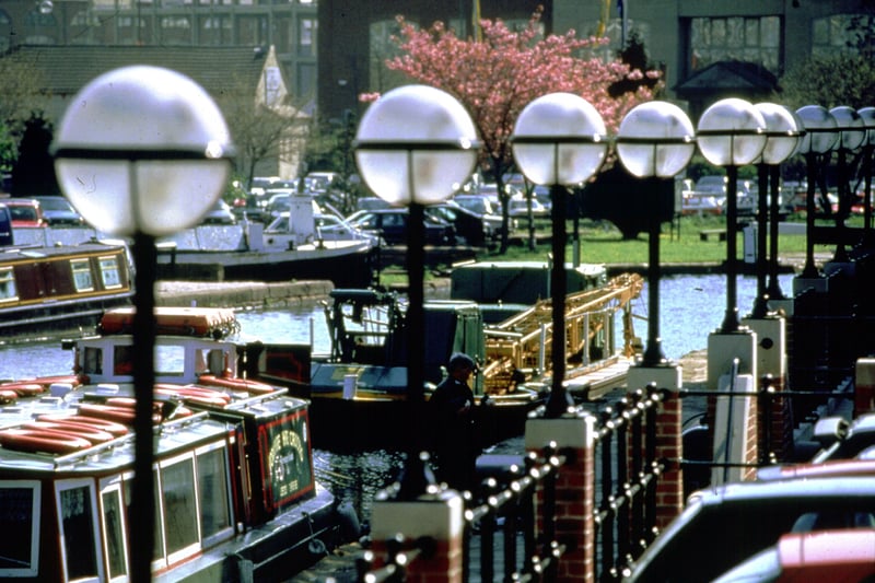 A view looking across the canal to the car park at Granary Wharf. The UKI Partnership building is in the background. Several barges are visible and decorative lighting dominates the foreground.