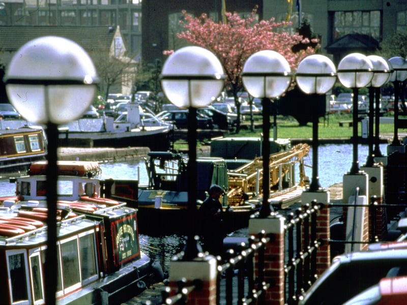 A view looking across the canal to the car park at Granary Wharf. The UKI Partnership building is in the background. Several barges are visible and decorative lighting dominates the foreground.
