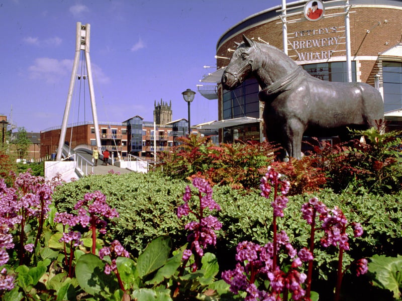 Tetley's Brewery Wharf Museum, right, which opened on March 19, 1994, beside the River Aire and closed in 2000. There is a sculpture of a Tetley's shire horse, and beyond Centenary Bridge accessing The Calls across the river. The tower of Leeds Parish Church of St. Peter, can be seen in the background