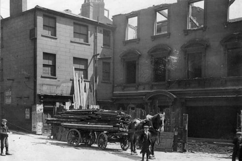 Bishopgate Street taken during improvement works. A partially demolished building is seen on the right; this was formerly the premises of Hepton Bros., mantle manufacturers. In the foreground, a horse-drawn cart bearing the name D. Milton of Sweet Street West, Holbeck, is loaded with wooden planks. Pictured in June 1899.