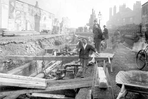 The building storm culvert in the vicinity of Hunslet's Church Street in October 1899. View of work area, pipes are marked 'gas' and 'water'. Workmen can be seen, with wheelbarrows, steam crane and other equipment.