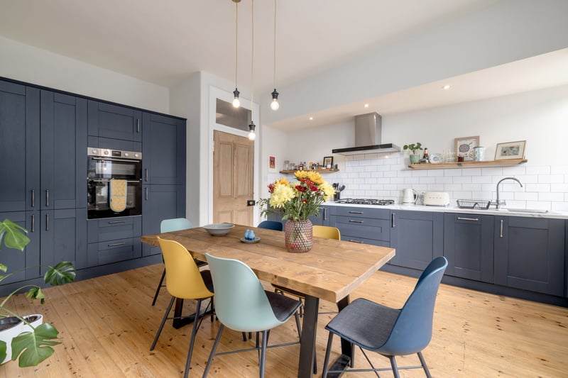 The magnificent, spacious open plan kitchen/dining room with two windows and an excellent range of navy shaker style fitted cupboards, integrated appliances, open wooden shelving and loads of space for a large dining table with feature lighting above.