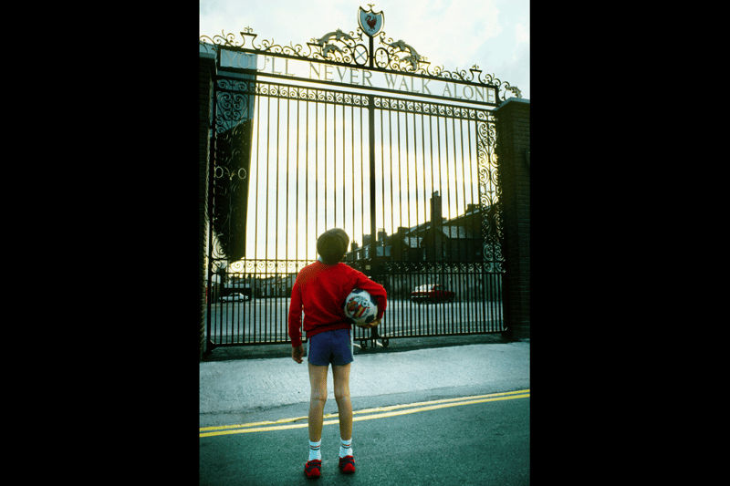 A young footballer looks up at the Shankly Gates with an Espana '82 World Cup football under his arm.