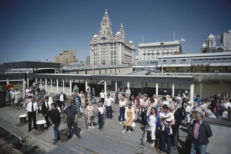 Crowds wait to board the Birkenhead ferry to cross the river Mersey, with the old terminal in the background.