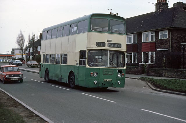 A green double decker bus approaches Speke Road's junction with Banks Road. Despite regeneration of the area, the houses on the right survive though the petrol station on the left of the photo has disappeared. 